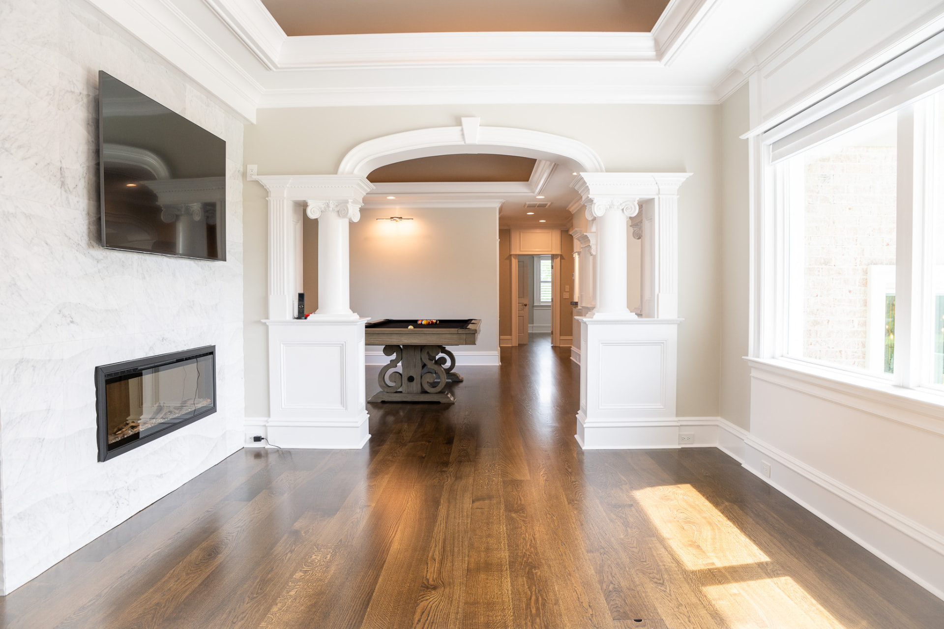 Game Room & Column Screen — Elliptical arch on paired columns, tray ceilings and wire-brushed oak flooring through the lower level.