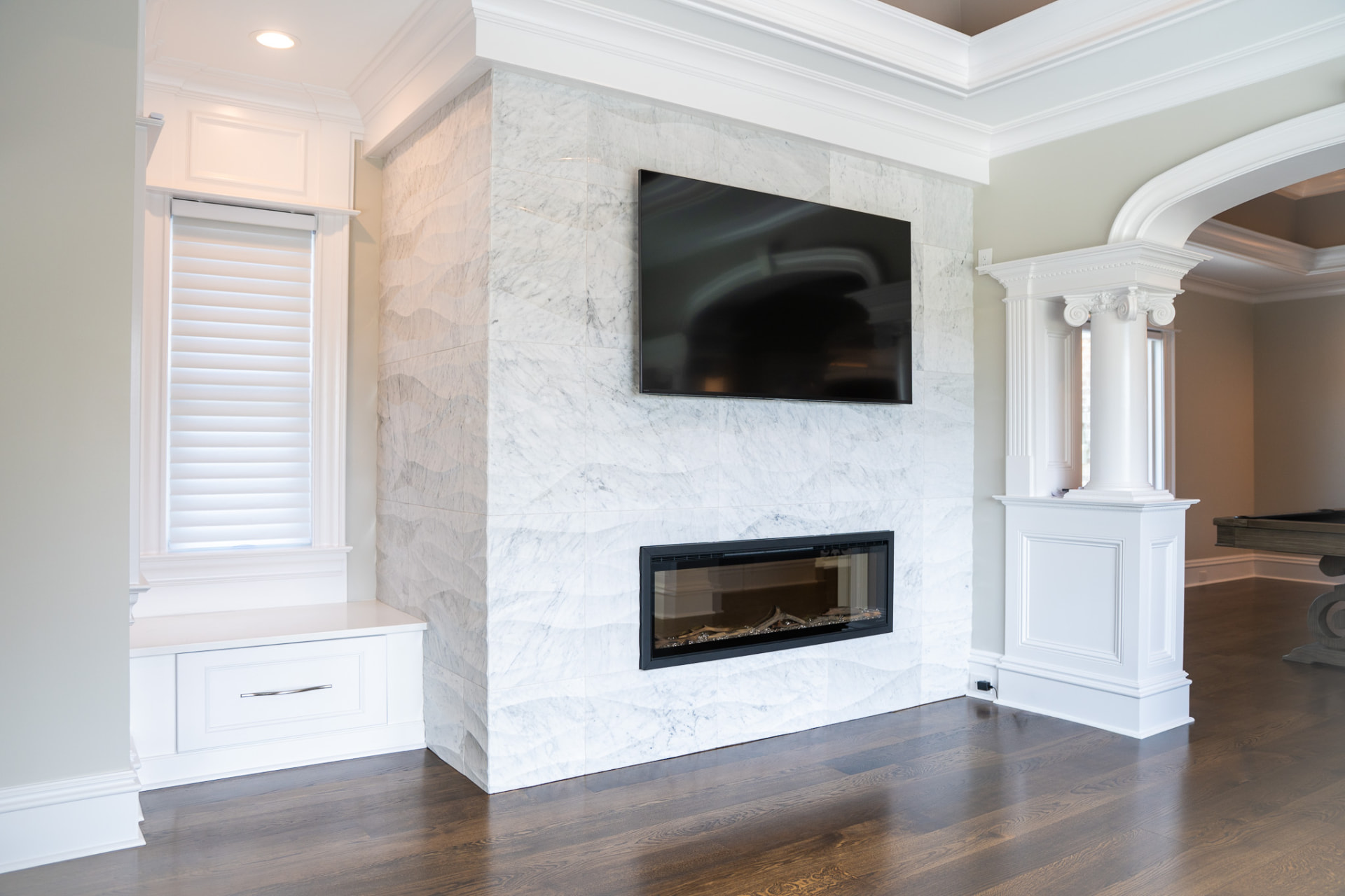 Marble Fireplace Wall — Dimensional marble surround with a linear fireplace, window seat storage and columned opening to the game room.