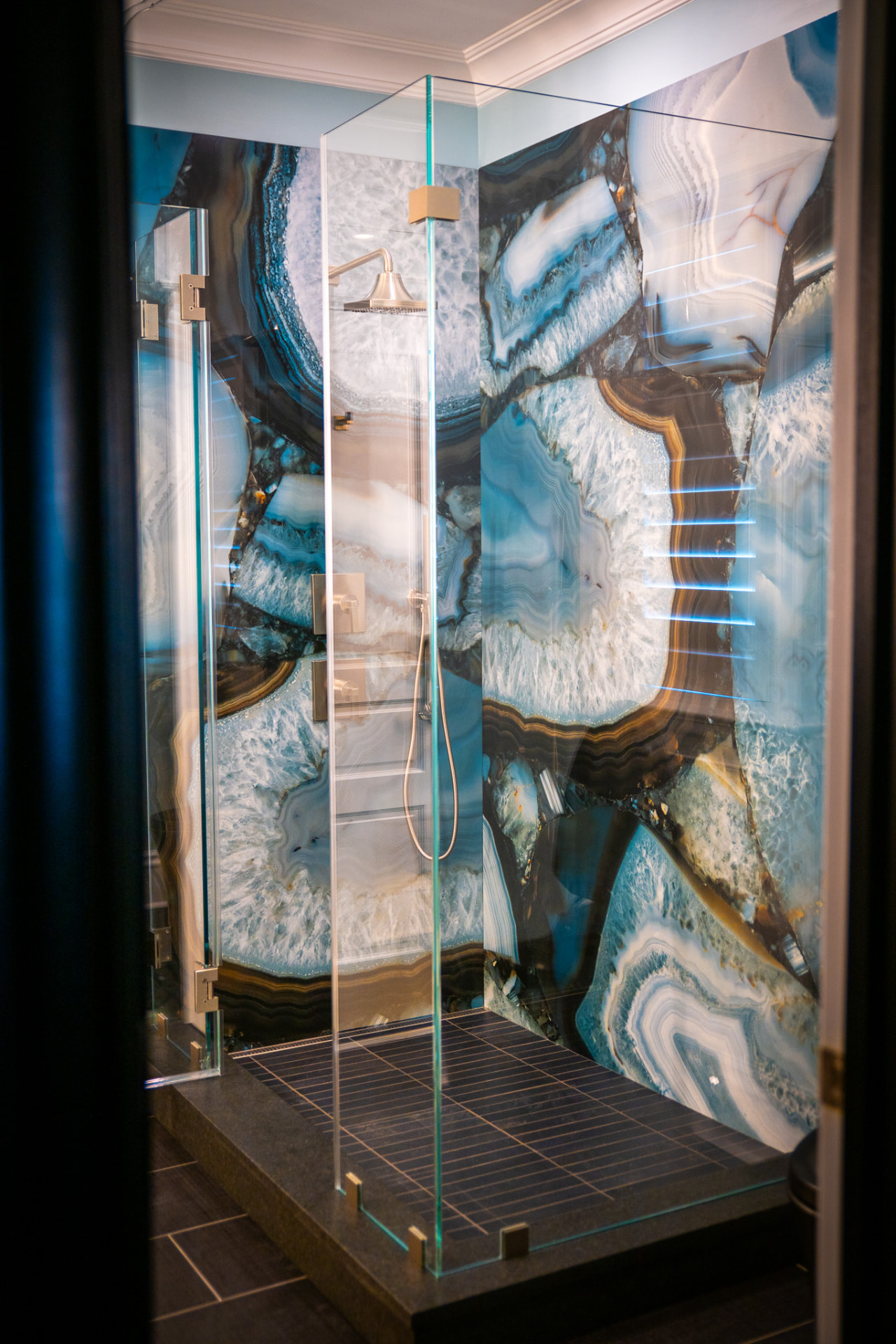Agate Guest Shower — Backlit agate panels, frameless glass and a stone curb set over a fine-format tile floor.