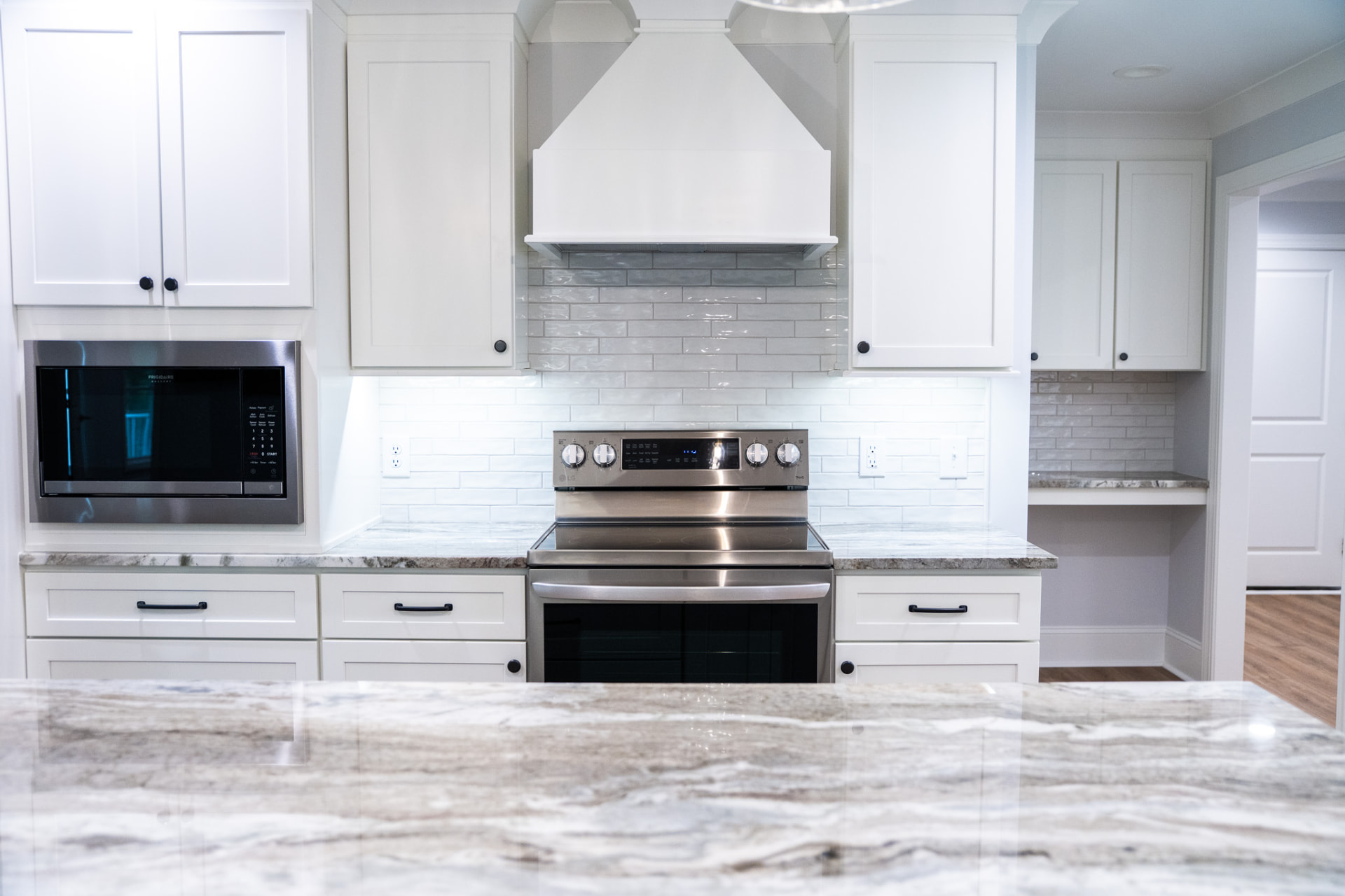 Range Wall & Backsplash — Handmade tile backsplash, integrated microwave cabinet and a mitred stone counter return at the desk niche.