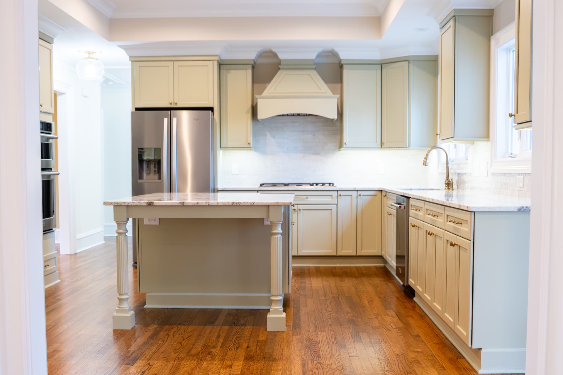 Sage Kitchen Renovation — Painted cabinetry with a furniture-style island, arched hood surround and stone tile backsplash over red oak floors.