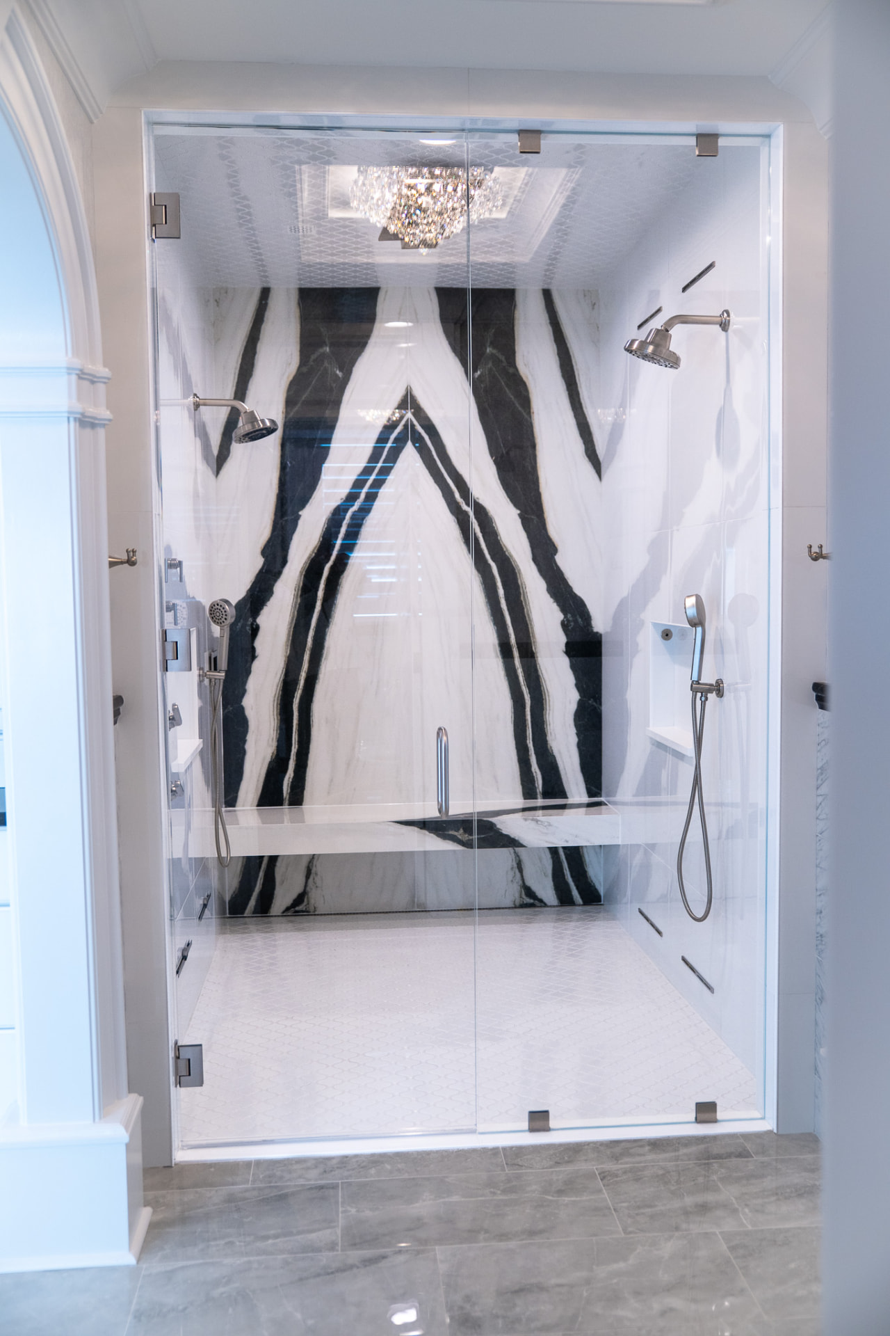 Book-Matched Stone Shower — Book-matched marble feature wall, full glass enclosure, built-in bench and a multi-head fixture layout.