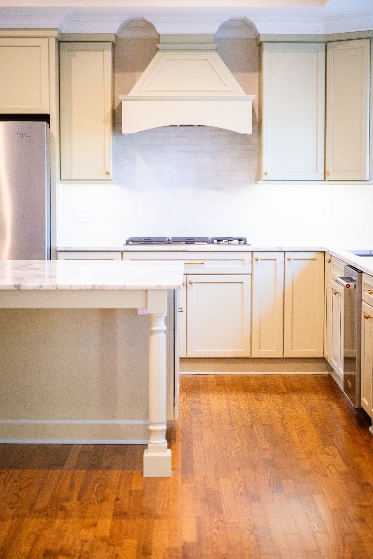 Traditional Kitchen — Raised-panel cabinetry, a furniture-leg island and marble counters over site-finished red oak flooring.