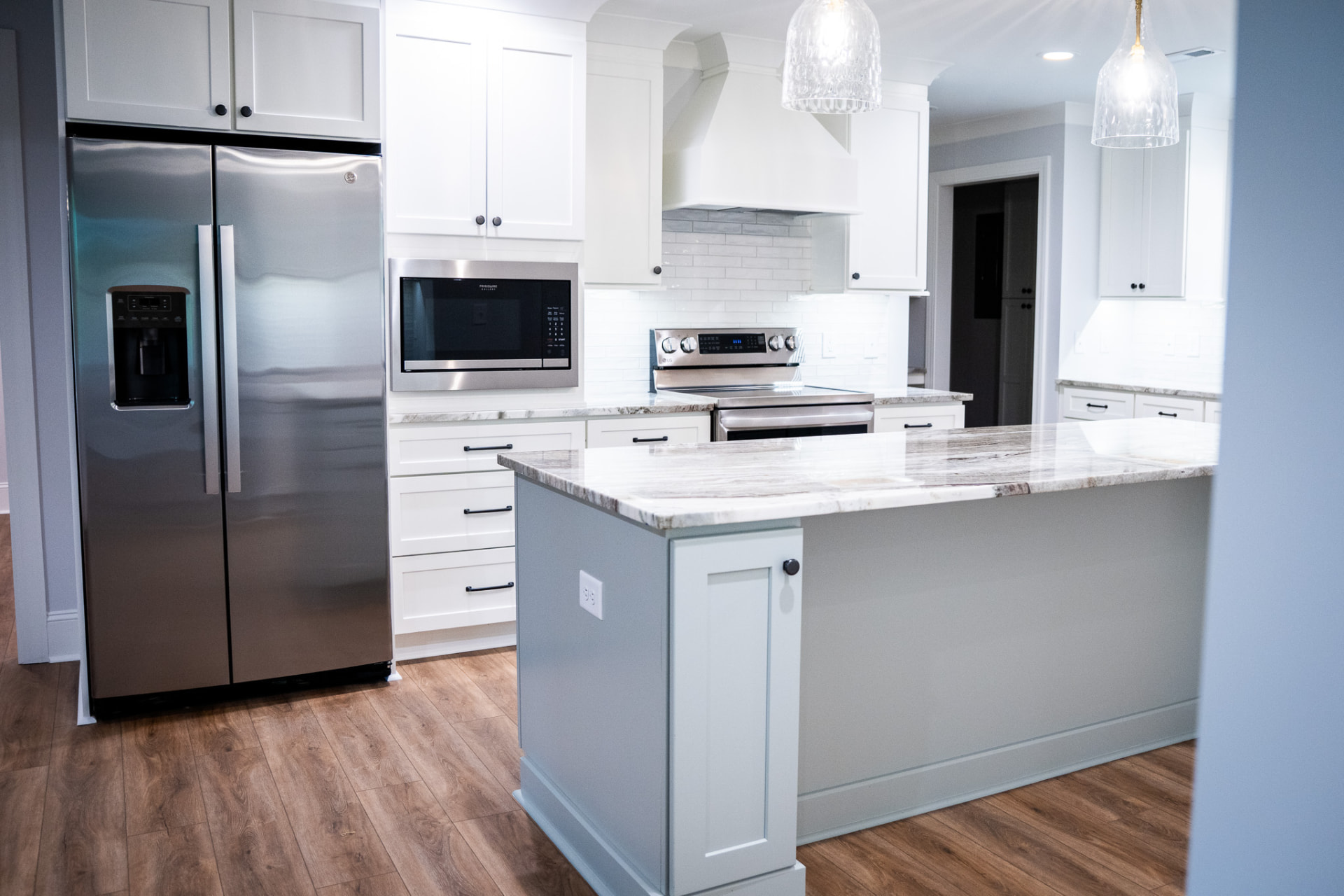 Kitchen Island & Peninsula — Full-height cabinetry, custom hood surround and a veined quartzite peninsula under glass pendants.