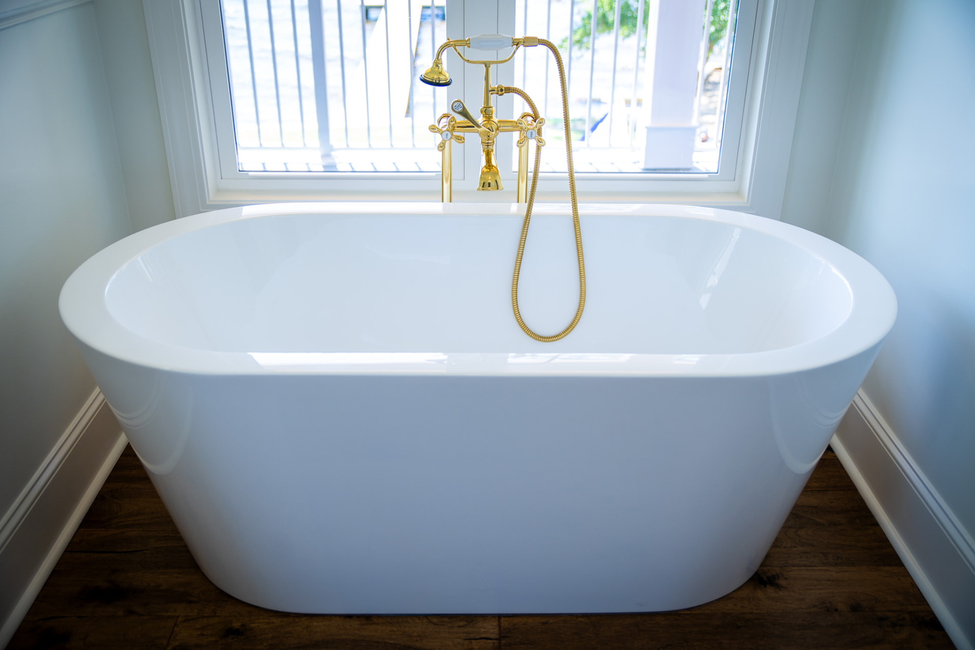 Freestanding Soaking Tub — Freestanding tub set into a trimmed window alcove with a polished brass floor filler and wide-plank flooring.