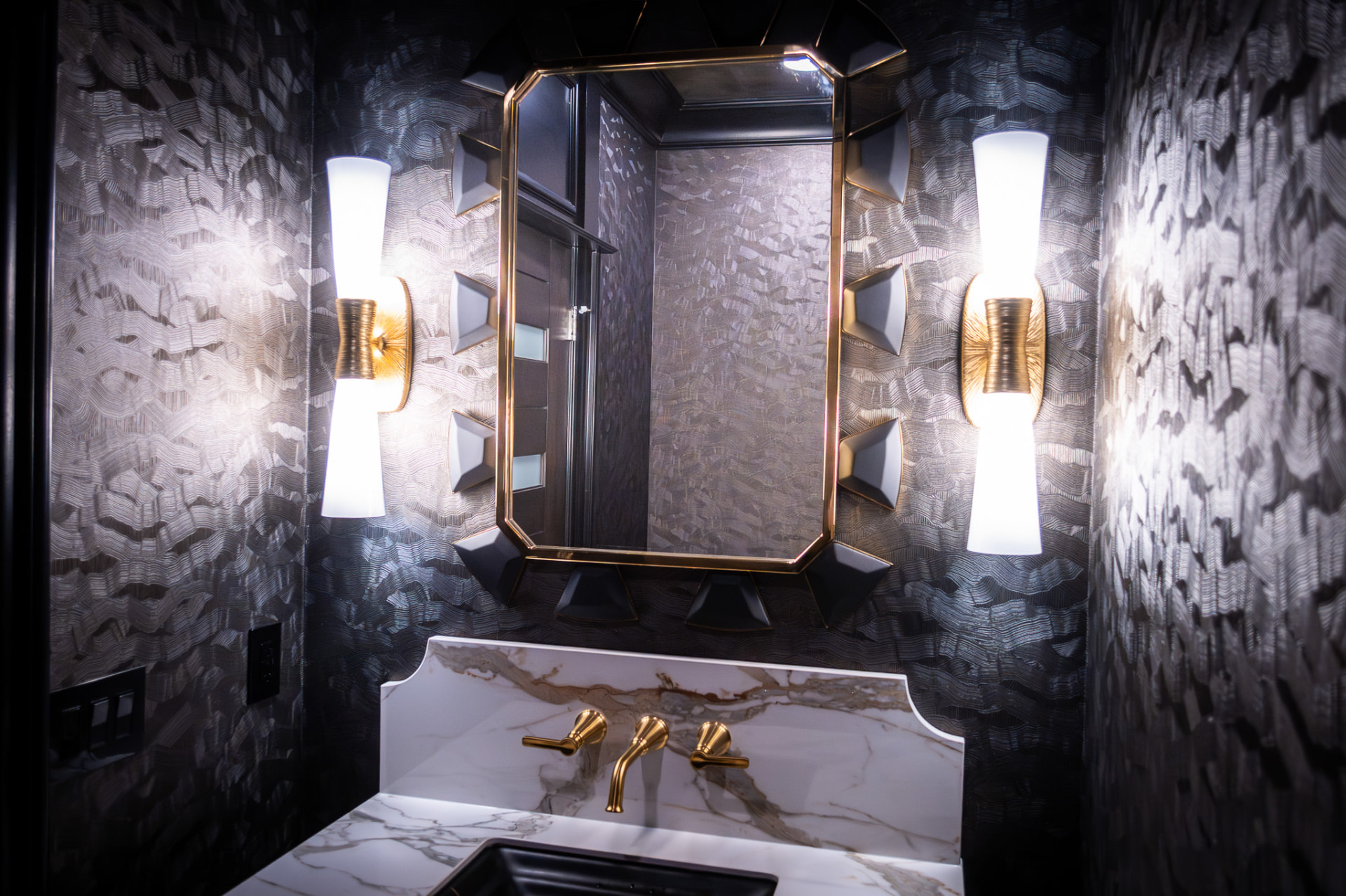 Powder Room — Marble vanity with unlacquered brass fittings, a faceted mirror and a dark textured wallcovering in a compact powder room.