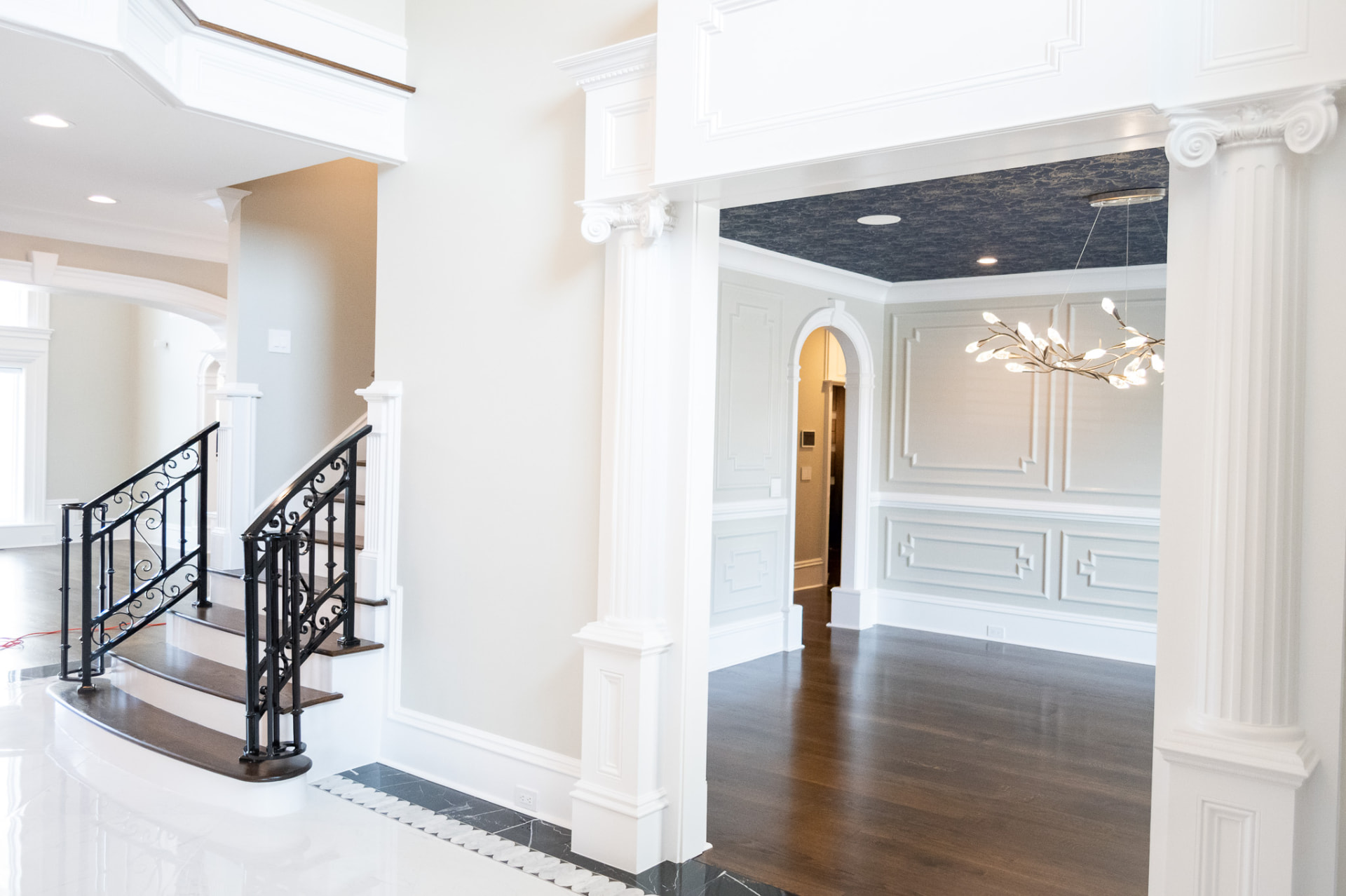 Foyer & Formal Dining — Ionic column screen, curved stair with iron balustrade and applied wall panelling framing a papered dining ceiling.